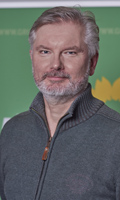 Porträt eines grauhaarigen Mannes mit Vollbart vor einer Plakatwand der Partei Die Grünen